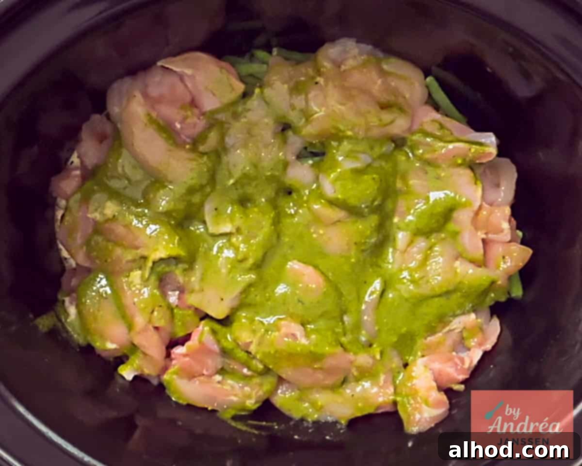 Slow Cooker Creamy Tuscan Pesto Chicken 5 Spreading pesto evenly over the chicken strips in the slow cooker, ensuring maximum flavor infusion.